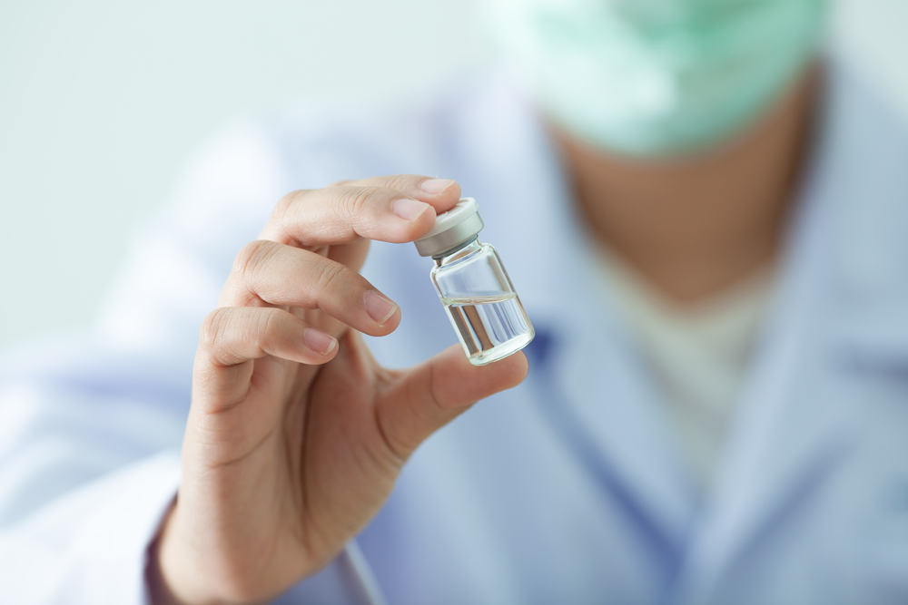 Healthcare professional holding a small glass vial containing a clear liquid, symbolizing vaccine preparation or medication, in a laboratory setting.