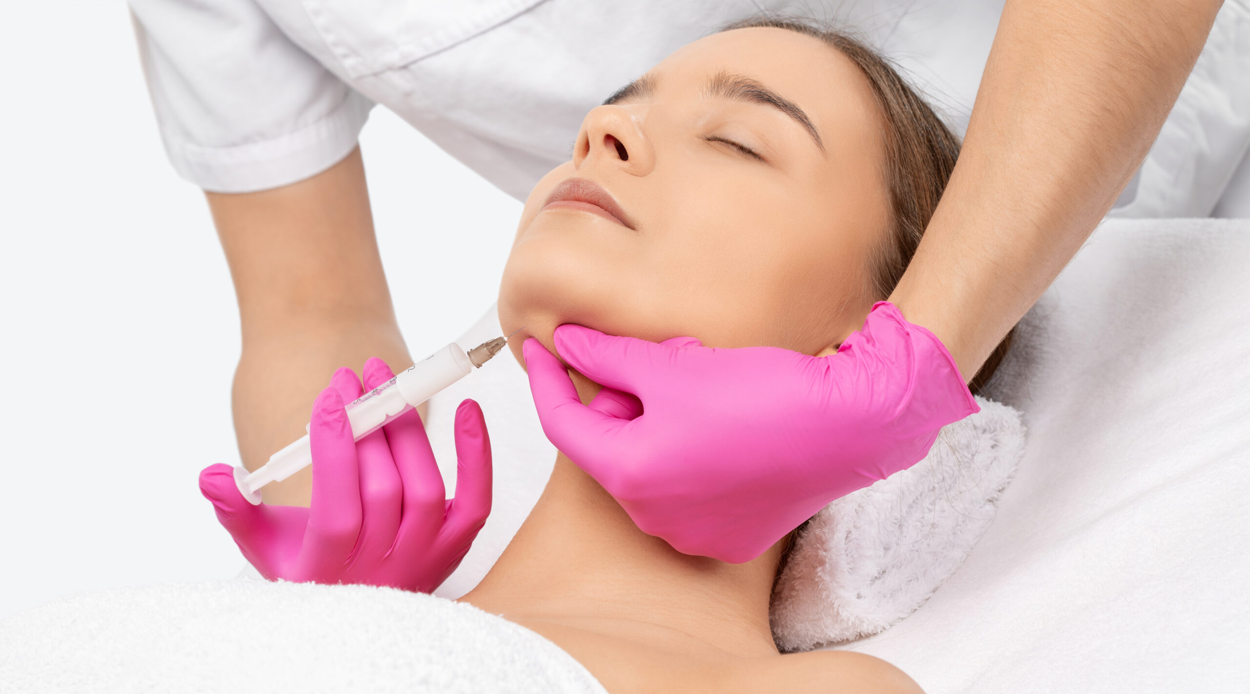 Aesthetic treatment session with a professional applying an injectable filler to a woman's chin, showcasing skincare and beauty procedures.