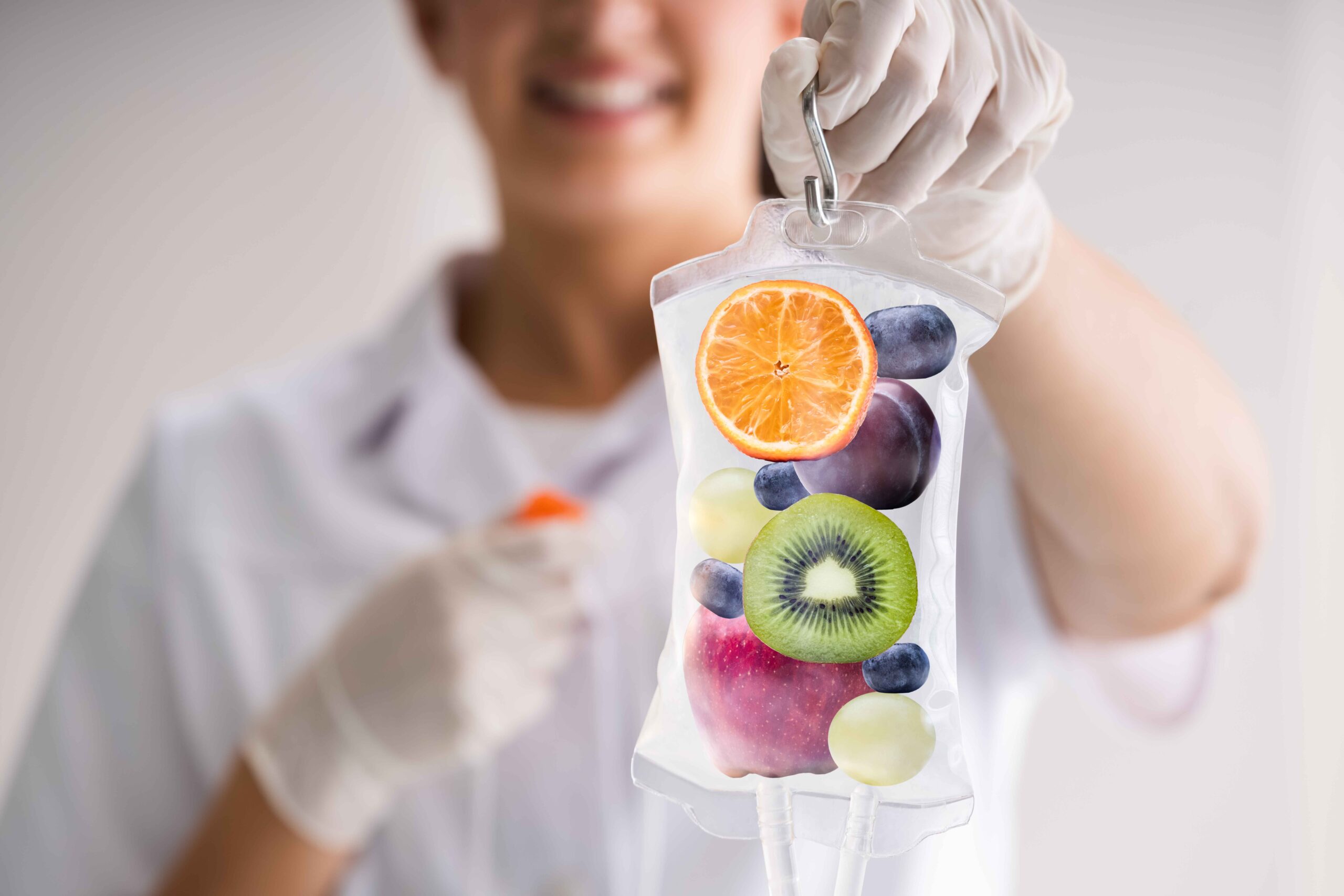 Healthcare professional holding an IV bag filled with fresh fruits like oranges, kiwis, and apples, symbolizing vitamin infusion therapy and wellness.