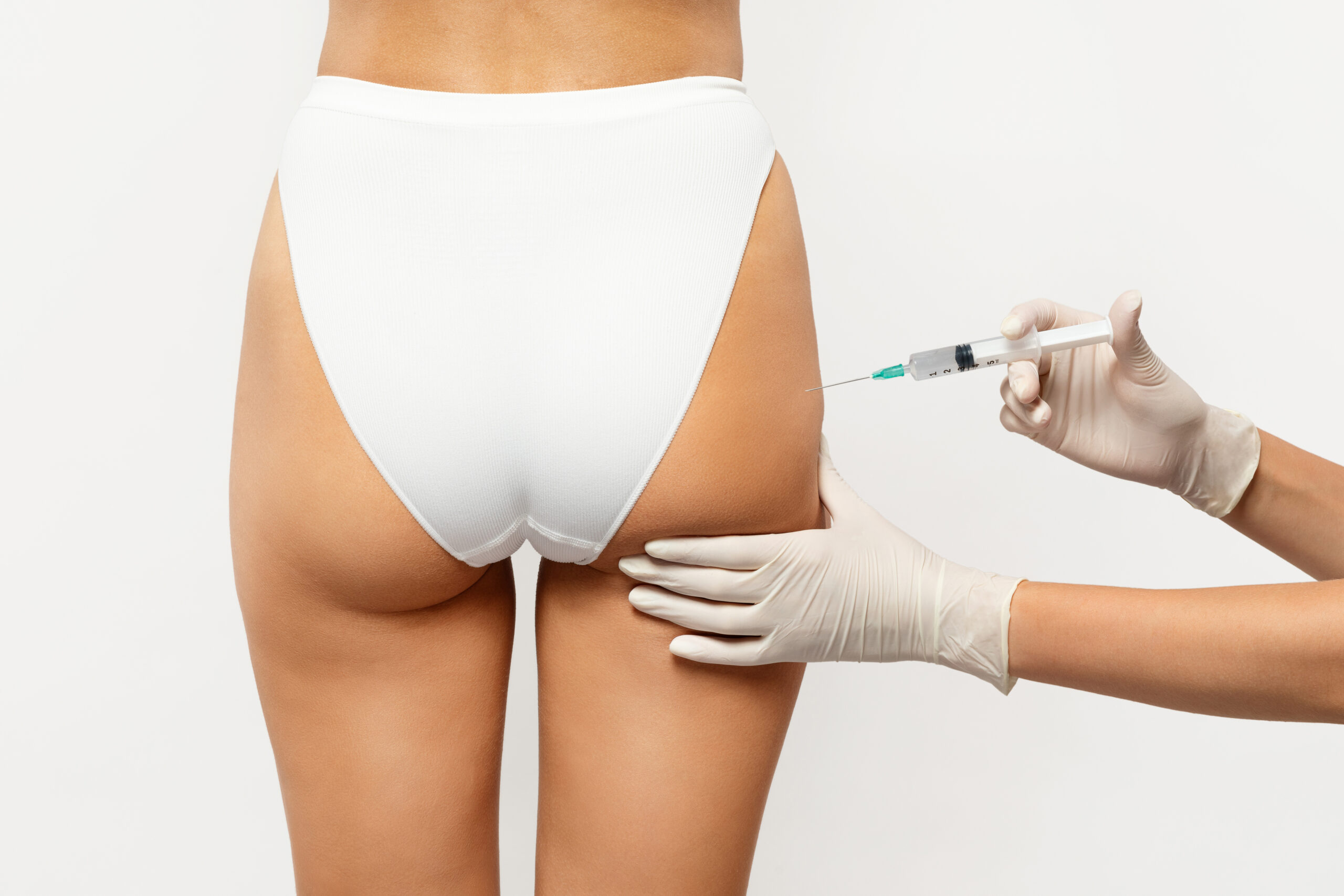 Injection procedure in cosmetology, focusing on a woman's buttocks, highlighting a syringe being administered by a gloved hand.
