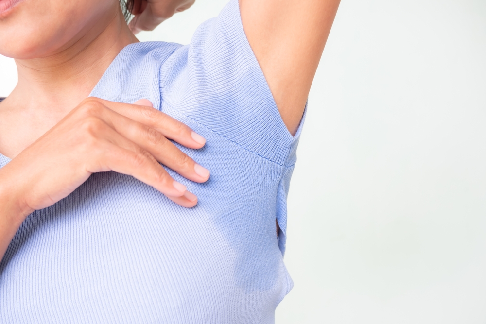 Close-up of a person adjusting their clothing under the arm, showcasing sweat stains on a light blue shirt, highlighting issues related to body odor and sweat management.