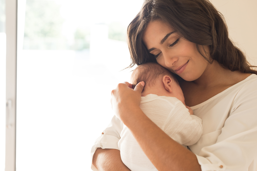 Mother lovingly cradles her newborn baby, showcasing a tender moment of connection and affection in a bright, softly lit room.