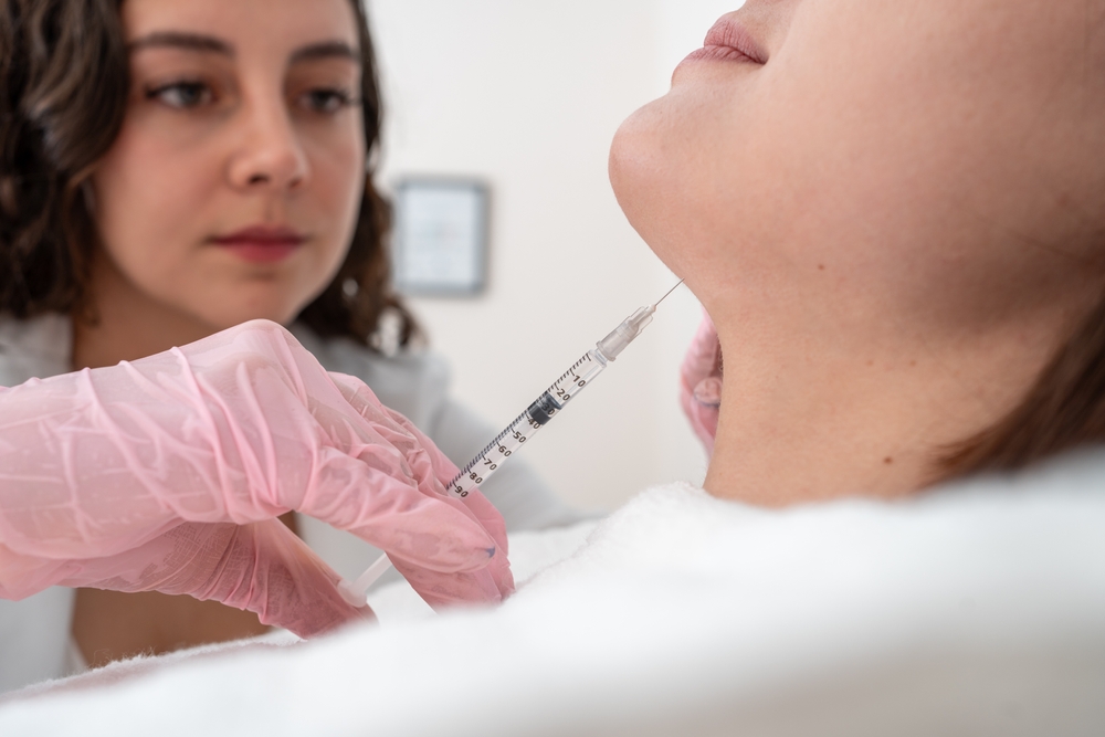 Close-up of a healthcare professional administering an injection to a patient's chin during a cosmetic procedure, highlighting the use of a syringe and sterile techniques in a clinical setting.