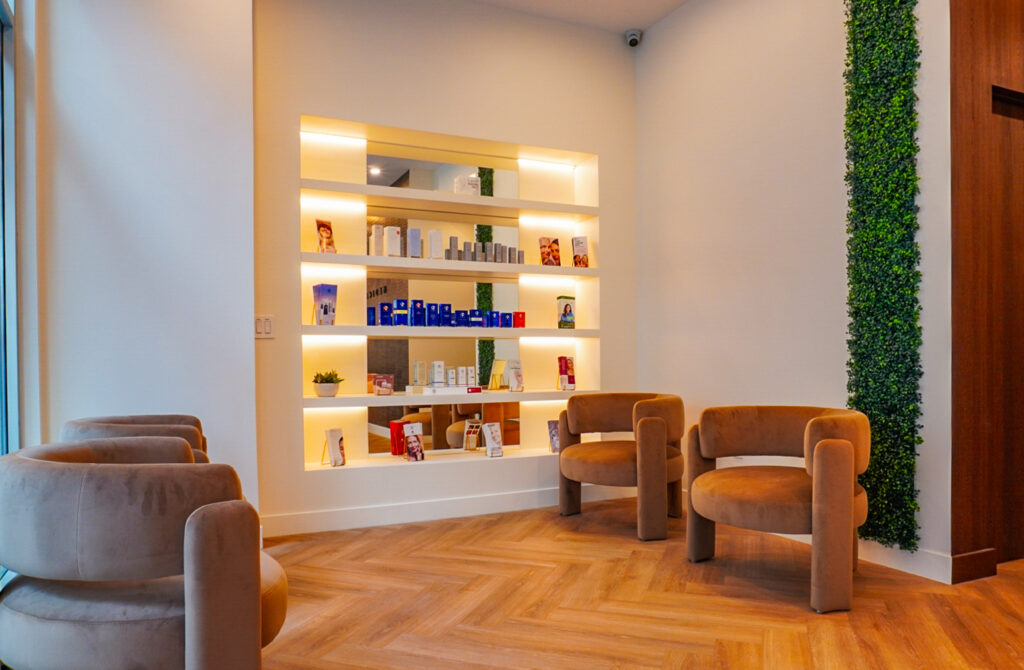 Modern aesthetic interior of a wellness clinic featuring a display shelf with skincare products, a cozy seating area with plush chairs, and wooden flooring.