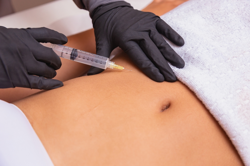 A healthcare professional in black gloves performs an injection on a patient's abdomen, illustrating a cosmetic or medical procedure.